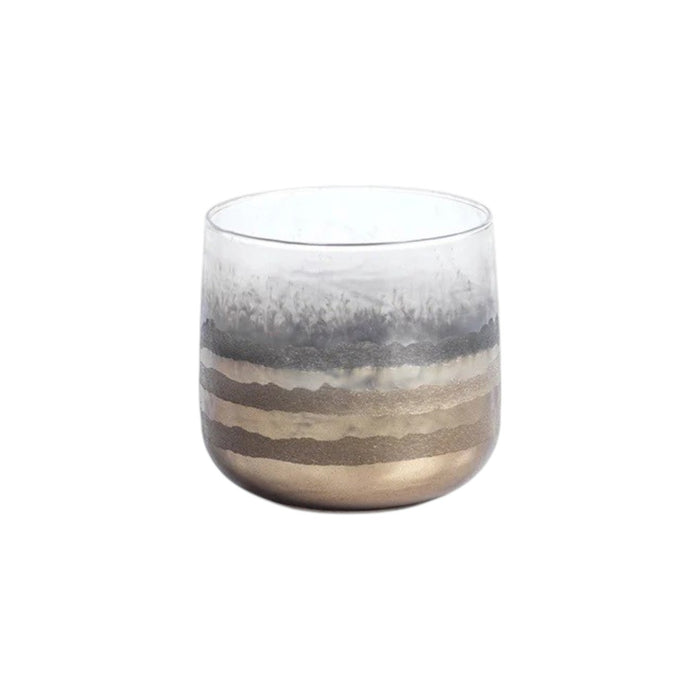 Three ZODAX GOLD SMOKE VOTIVE HOLDERS, featuring a hand-applied finish of metallic and frosted horizontal stripes, each with a lit candle inside, are arranged on a white surface against a yellow background, casting a warm metallic glow.