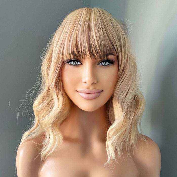 Woman with blonde wavy hair and bangs against a neutral background