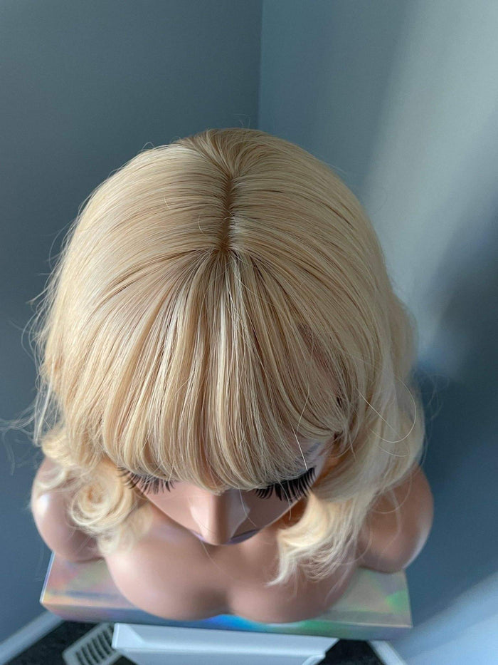 Blonde wig on a mannequin head against a neutral background