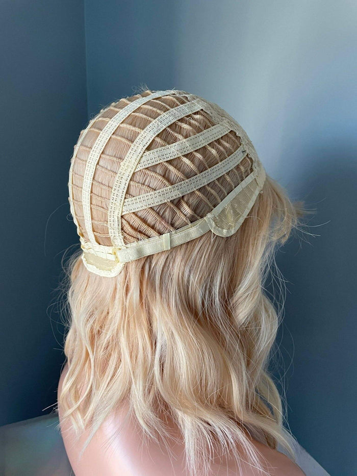 Person wearing a blonde wig with a mesh cap against a blue background