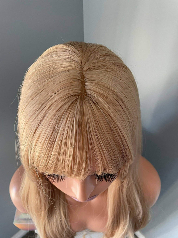 Blonde wig on a mannequin head against a neutral background