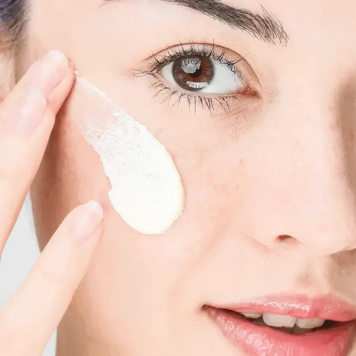 Woman applying cream to her face with a neutral background