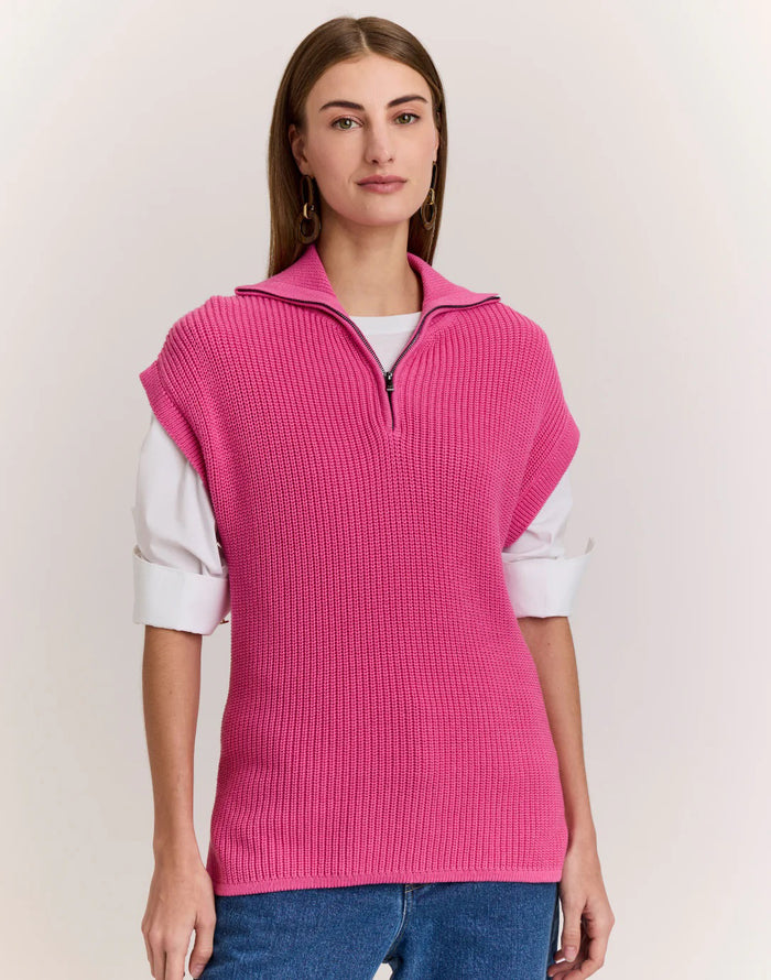 A woman with straight brown hair wears the HINSON WU BROOKE Sleeveless Knit Vest in bright pink over a white shirt and blue jeans, standing against a plain light background.
