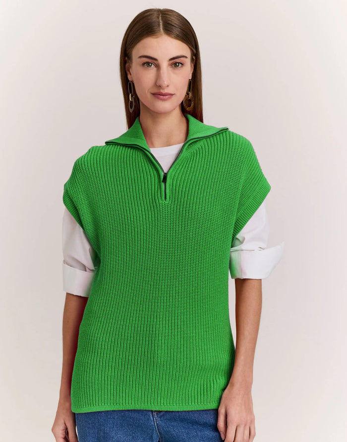 A woman wears the HINSON WU - BROOKE SLEEVELESS KNIT VEST in bright green over a white long-sleeve shirt and blue jeans, standing against a plain light background.