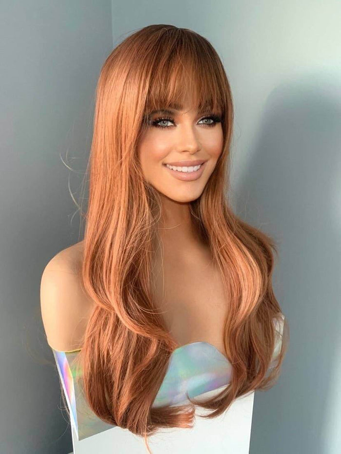 Jordan Auburn Wig with Bangs featuring long wavy hair and a beautiful full fringe.