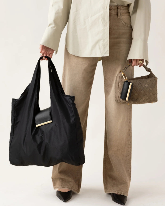 The KEOTE - KEYCHAIN TOTE IN JET BLACK by KEOTE is a reusable black tote made of crinkled fabric, shown flat with a matching small carrying case—ideal as a compact bag for easy storage and daily use.