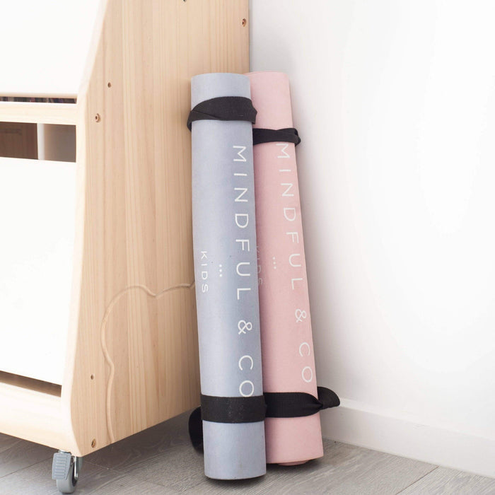 Two yoga mats, one gray and one pink, with 'Mindful & Co' branding, leaning against a wooden piece of furniture.
