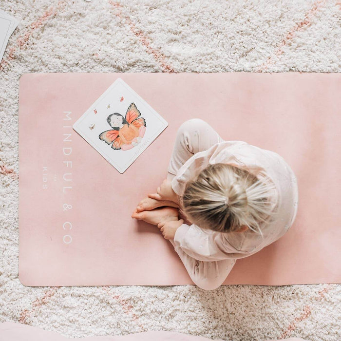 Person sitting on a pink 'MINDFUL & CO' mat with a butterfly card on a textured surface