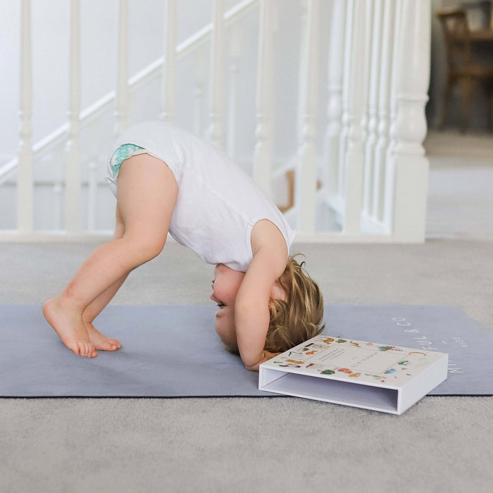 Child doing a handstand on a yoga mat with a book open next to them in a home setting.