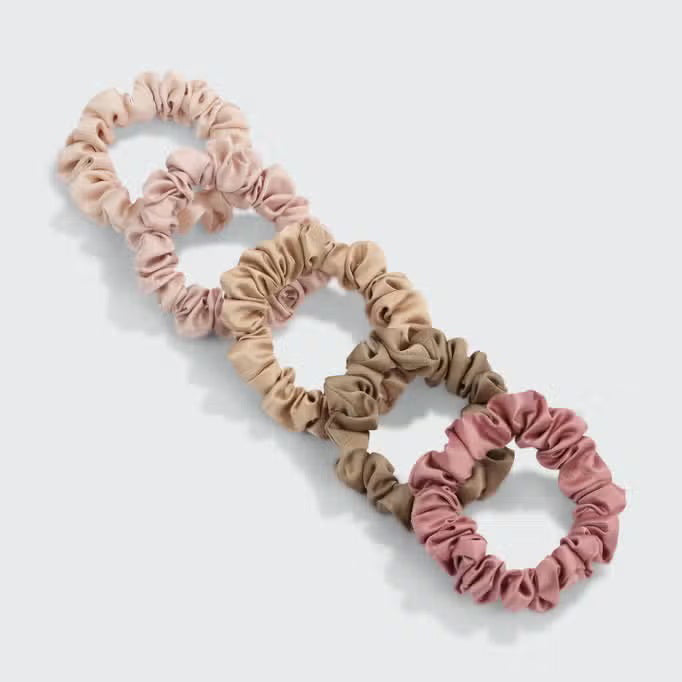 A set of six eco-friendly KITSCH - ULTRA PETITE SATIN SCRUNCHIES in elegant pink and beige shades is displayed on a branded card. These scrunchies not only enhance your style but also help reduce hair damage, making them both chic and gentle on your hair.