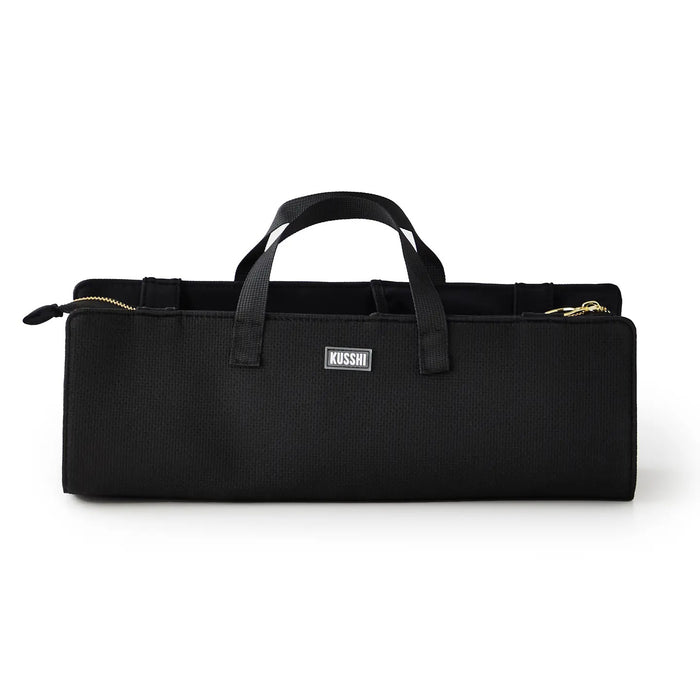 The KUSSHI - HAIR TOOLS TRAVEL BAG IN BLACK by KUSSHI is a rectangular neoprene organizer with two handles, gold zippers, and a white front label, shown against a white background.
