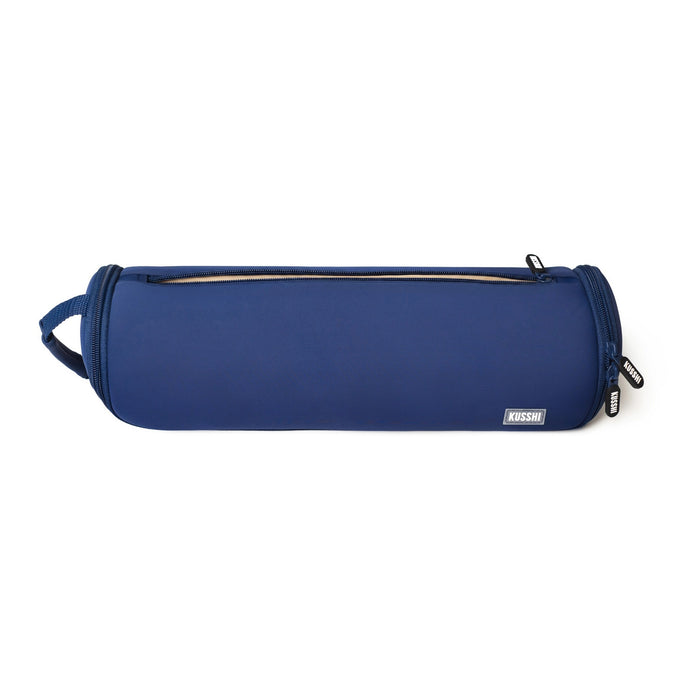 A hand with painted nails and a jade bangle holds the KUSSHI - Hair Tools Travel Case in Navy by its handle against a plain white background.