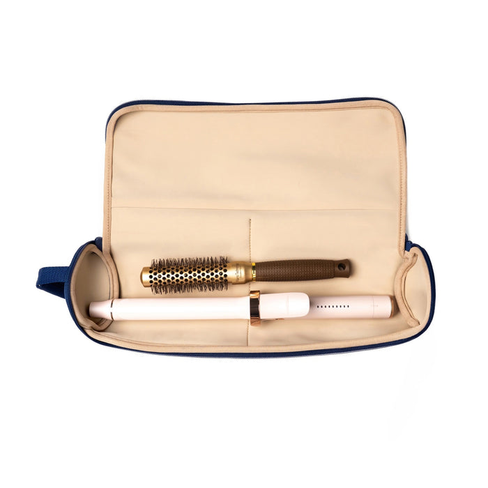 A hand with painted nails and a jade bangle holds the KUSSHI - Hair Tools Travel Case in Navy by its handle against a plain white background.