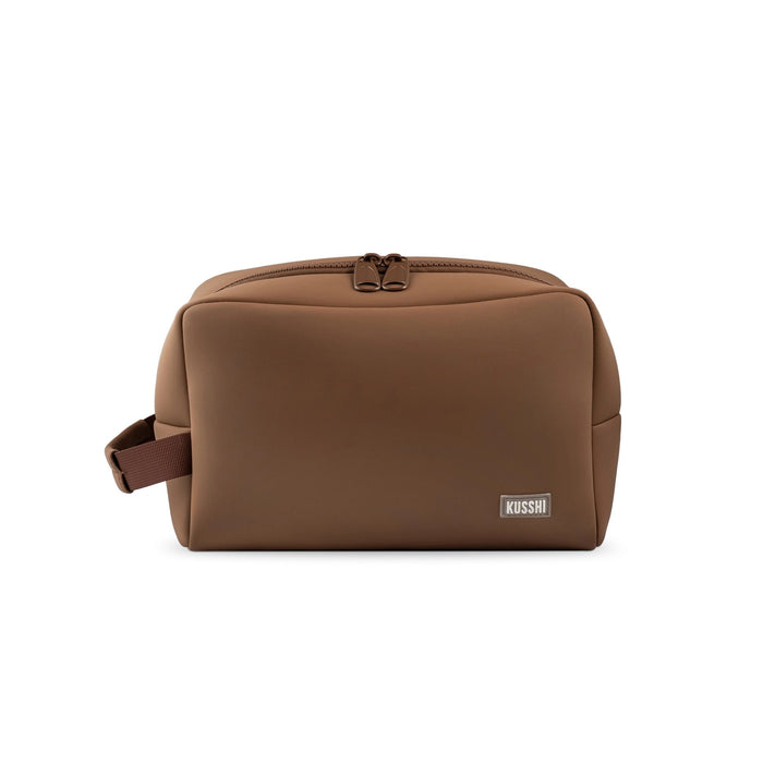 The KUSSHI Neoprene Dopp Kit in Chocolate is a stylish unisex toiletry bag with a blue zipper, perfect for organizing grooming essentials like razors, soap, combs, and lotions while you travel.