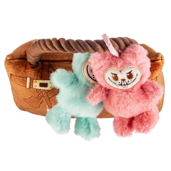 A French Bulldog sits indoors in a bright, cozy room, holding the HAUTE DIGGITY DOG LABOWWOW HANDBAG DOG TOY—a durable plush handbag adorned with pink and blue teddy bear keychains—in its mouth.