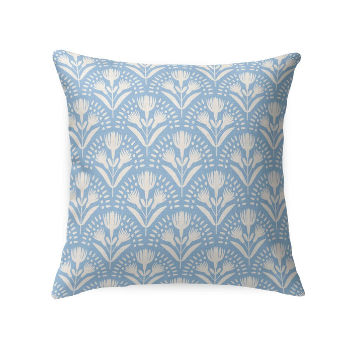 A wicker chair with a white cushion and a LOOM AND CLOTH - SERENA TAILORED PILLOW by LOOM & CLOTH sits next to a white nightstand with two vases, set against a wall featuring blue and white patterned wallpaper.