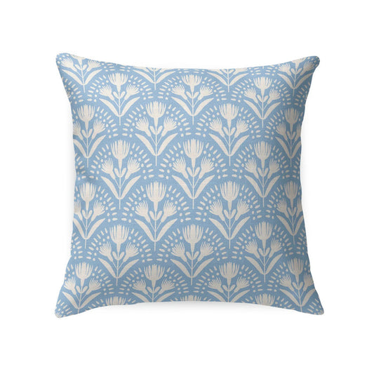 A wicker chair with a white cushion and a LOOM AND CLOTH - SERENA TAILORED PILLOW by LOOM & CLOTH sits next to a white nightstand with two vases, set against a wall featuring blue and white patterned wallpaper.