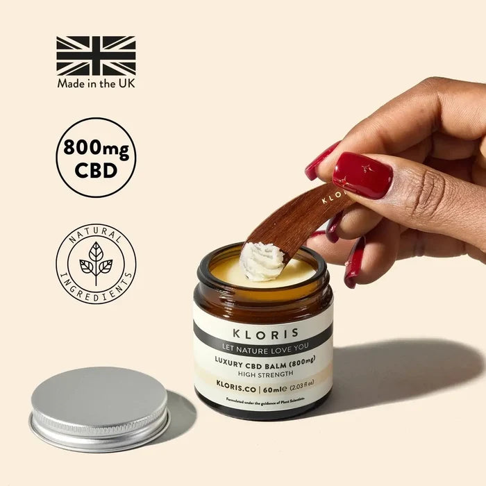 Hand applying CBD balm from a jar labeled 'Kloris' with branding elements on a beige background.