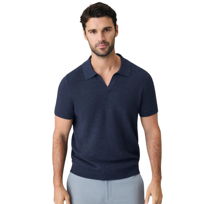 A close-up of a person’s arm and torso wearing the MACK WELDON Tech Linen Johnny Collar Polo Sweater in Navy Heather, paired with light gray pants featuring a buttoned pocket.