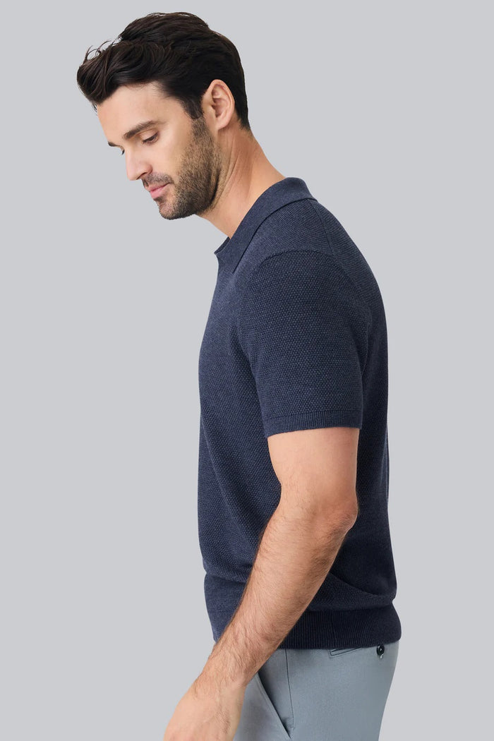 A man with short dark hair is seen from behind wearing the MACK WELDON Tech Linen Johnny Collar Polo Sweater in Sage Leaf Heather, paired with light gray pants against a plain light gray background.