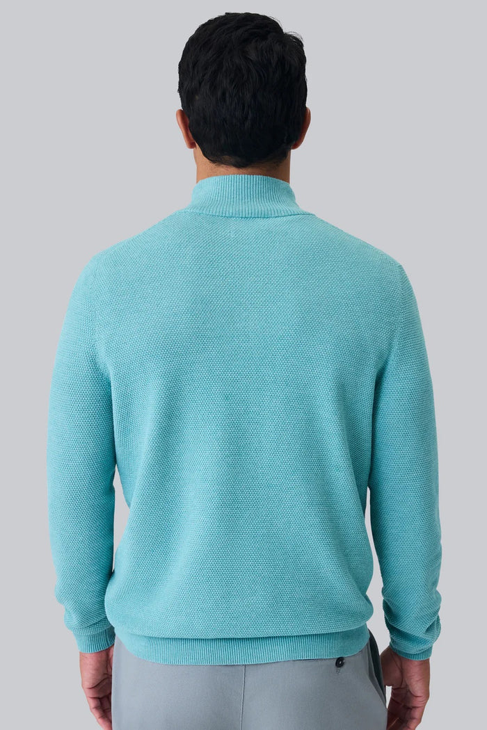 A man with short dark hair wears the MACK WELDON TECH LINEN QUARTER ZIP in Deep Lagoon Heather over a white shirt and light gray pants, standing against a plain white background with his hands loosely clasped.