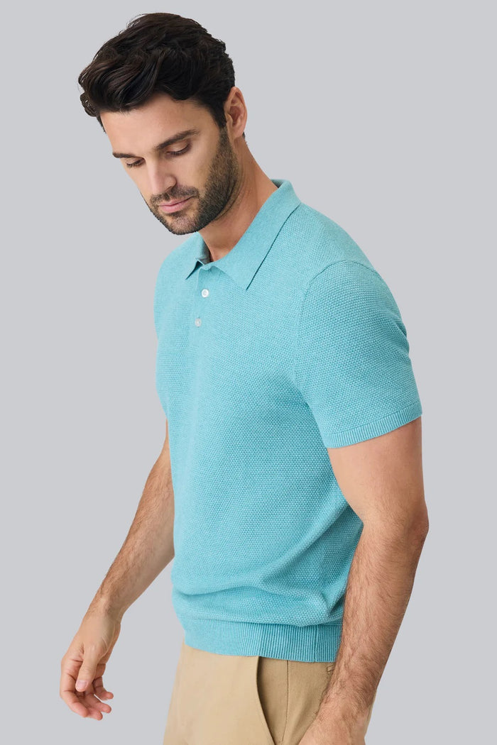 A man with short brown hair and a trimmed beard wears the MACK WELDON TECH LINEN SWEATER POLO in Deep Lagoon Heather and beige pants, standing against a plain white background.