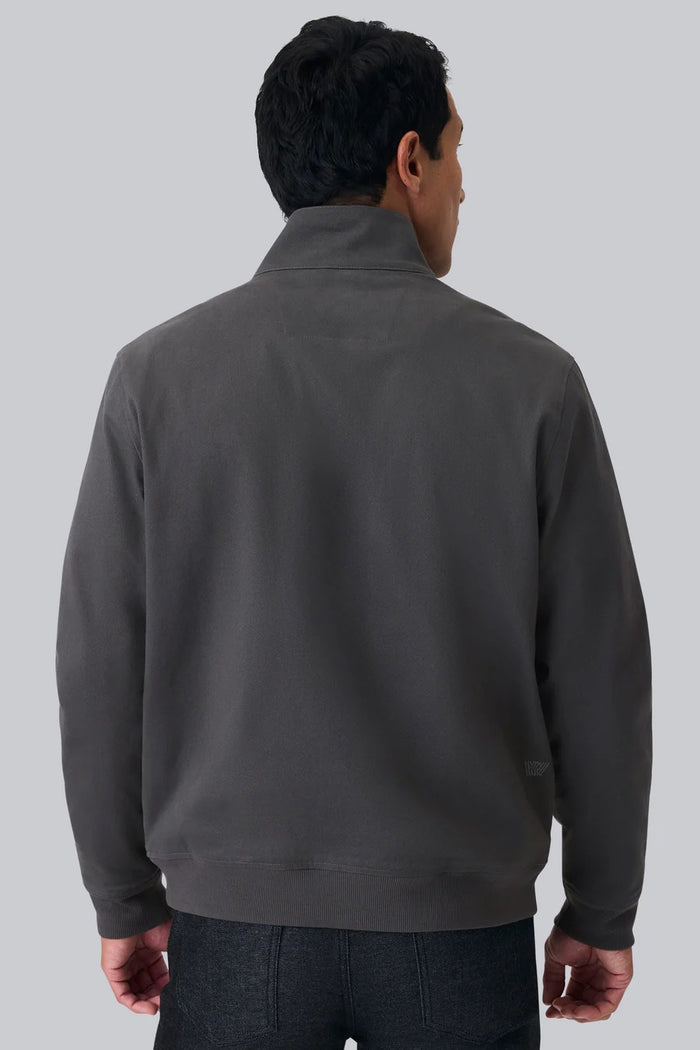 The MACK WELDON Twill Harrington Jacket in Asphalt is a dark gray cotton cavalry twill zip-up with a stand collar, two angled button-flap pockets, ribbed cuffs and hem, offering an English jacket style. Shown on a black background.