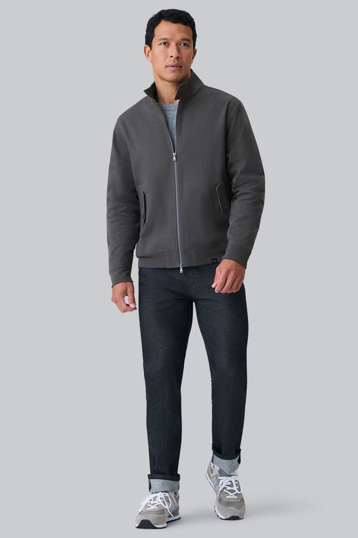 A man with short dark hair wears the MACK WELDON Twill Harrington Jacket in Asphalt over a gray shirt, standing against a light gray background and looking at the camera with a neutral expression.