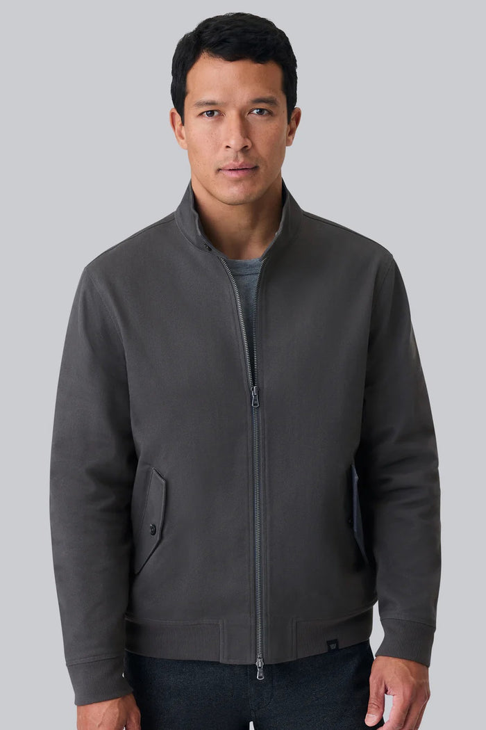 Close-up of a person wearing the MACK WELDON Twill Harrington Jacket in Shroom, featuring a zip front and buttoned flap pocket. Their arm is relaxed by their side and dark denim jeans are partially visible.