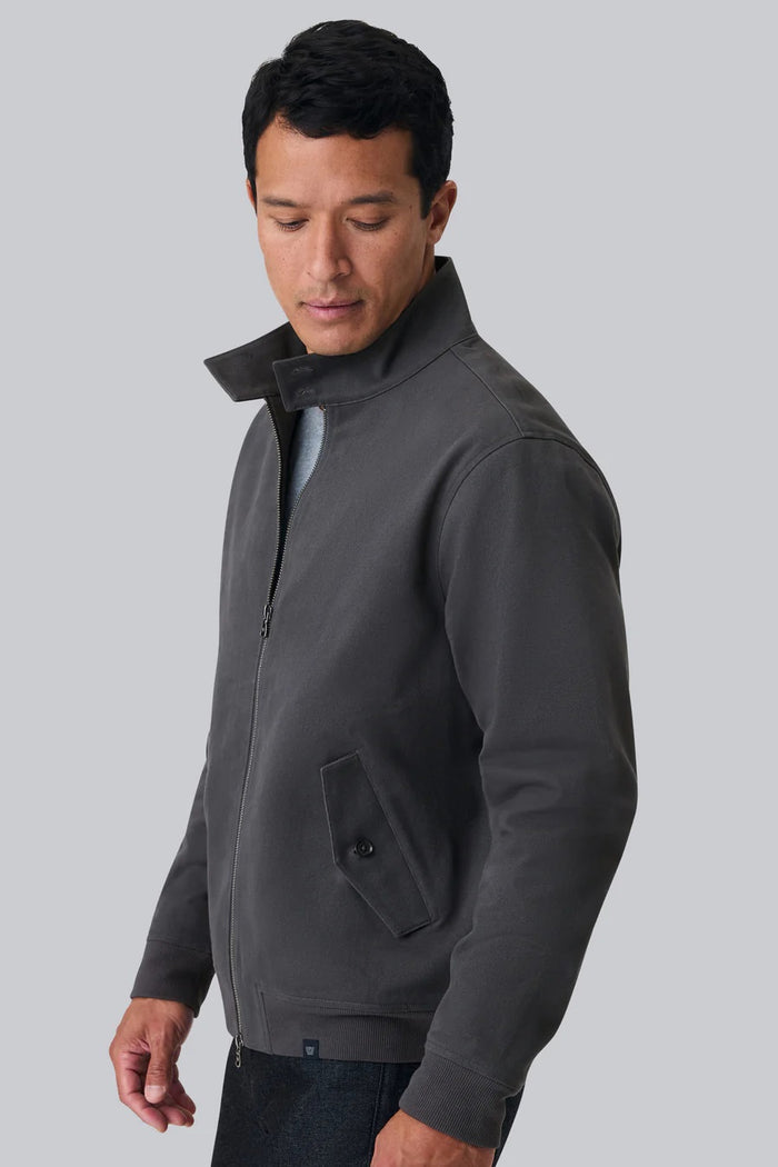 Close-up of a person wearing the MACK WELDON Twill Harrington Jacket in Shroom, featuring a zip front and buttoned flap pocket. Their arm is relaxed by their side and dark denim jeans are partially visible.