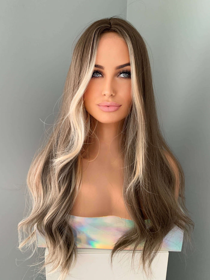Mannequin head with long, wavy brown and blonde wig against a gray background