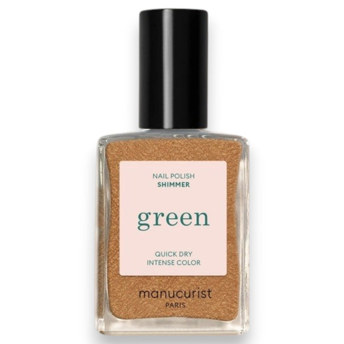 A hand adorned with metallic gold vegan nail polish holds a bottle of MANUCURIST - GREEN™ NAIL POLISH IN SHIMMER by MANUCURIST INC, set against a textured, light-filled background.