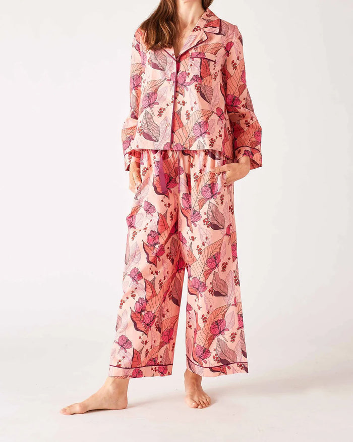 A woman stands barefoot in the MERSEA - OVER THE MOON PAJAMA SET, a 100% cotton ensemble by MERSEA with vibrant red, teal, and white vertical stripes and arrow patterns; she has her hands in her pockets and long hair over one shoulder.