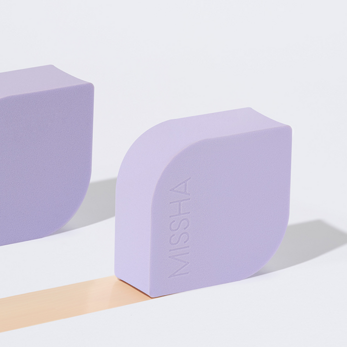 The MISSHA Layering Fit Puff resting on a surface, shown with a smooth, swatched trail of its peach-toned cream formula to demonstrate its blendable texture and coverage.