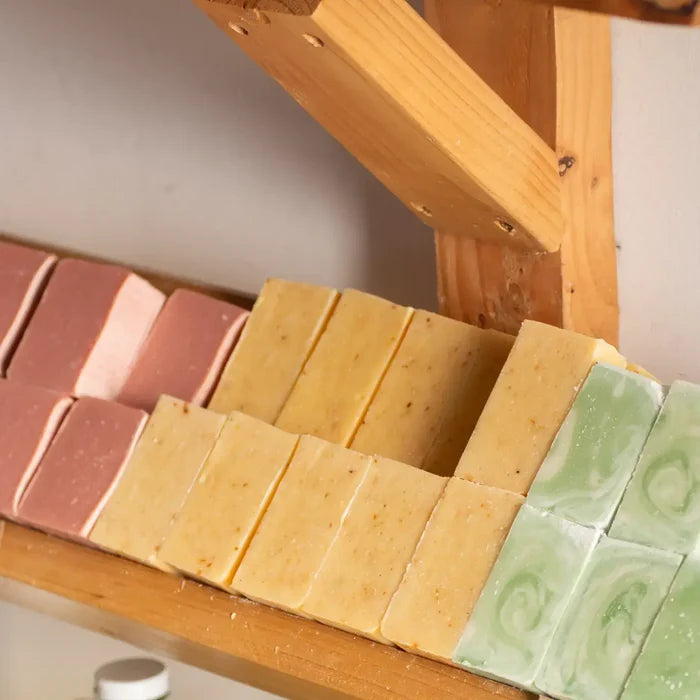 Assorted bars of soap on a wooden soap dish with a neutral background