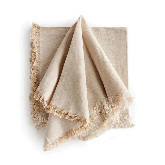 The NAPA HOME AND GARDEN - AURA Dinner Napkin in taupe is a square cotton napkin with fringed edges, neatly folded and set on a white background. Machine washable for easy care.