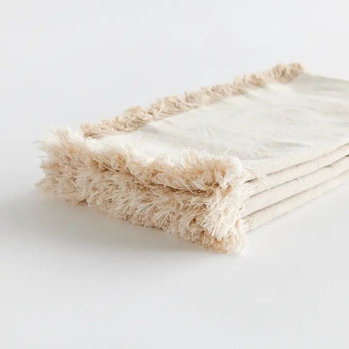 The NAPA HOME AND GARDEN - AURA Dinner Napkin in taupe is a square cotton napkin with fringed edges, neatly folded and set on a white background. Machine washable for easy care.