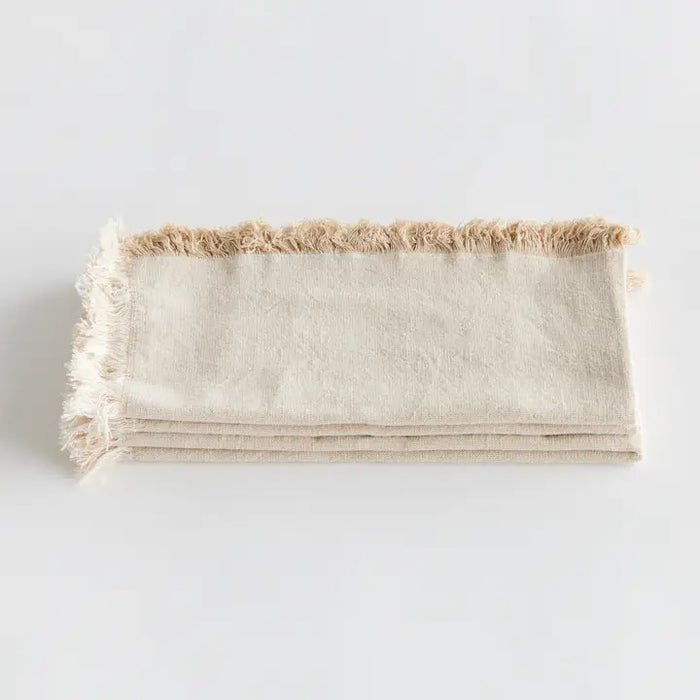 The NAPA HOME AND GARDEN - AURA Dinner Napkin in taupe is a square cotton napkin with fringed edges, neatly folded and set on a white background. Machine washable for easy care.