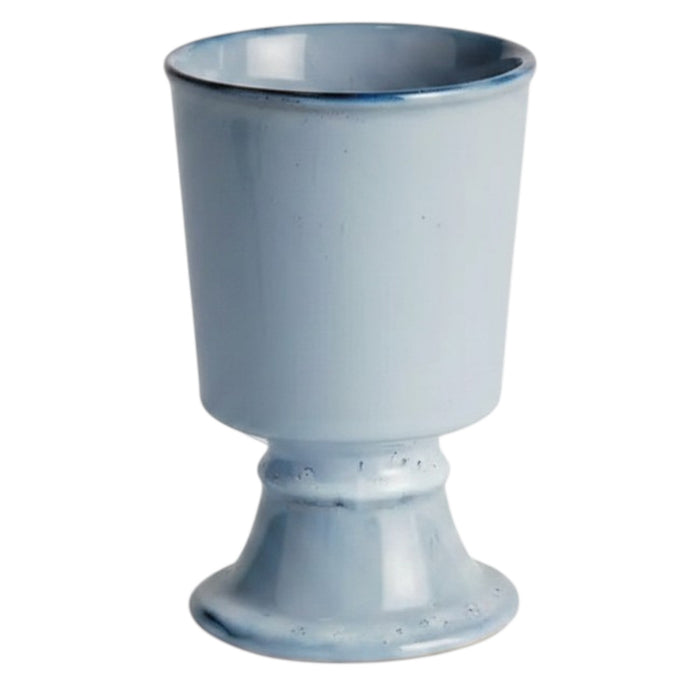 The NAPA HOME AND GARDEN Blue Kelcy Footed Cachepot, Small features a light blue ceramic finish with a glossy reactive glaze, subtle darker speckles near the rim and base, plus a wide rim and sturdy flared foot for a classic look.