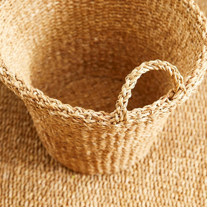 The NAPA HOME AND GARDEN Seagrass Tapered Basket with Handles and Cuff, Large, is shown from above, highlighting its natural seagrass texture and expert craftsmanship on a matching surface.