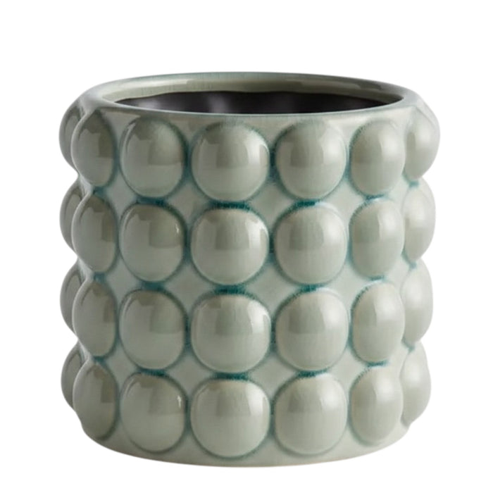 The NAPA HOME AND GARDEN - VALENCIA POT, LARGE is a round ceramic planter by NAPA HOME AND GARDEN, featuring a glossy seafoam glaze and a raised, bubble-like pattern on the exterior. This contemporary planter is light grey-green in color and is shown empty against a white background.