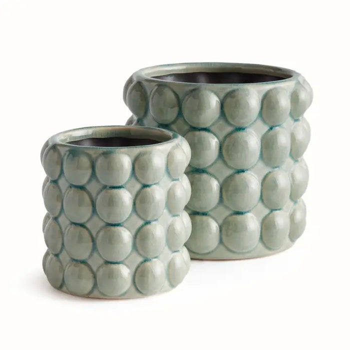 The NAPA HOME AND GARDEN - VALENCIA POT, LARGE is a round ceramic planter by NAPA HOME AND GARDEN, featuring a glossy seafoam glaze and a raised, bubble-like pattern on the exterior. This contemporary planter is light grey-green in color and is shown empty against a white background.