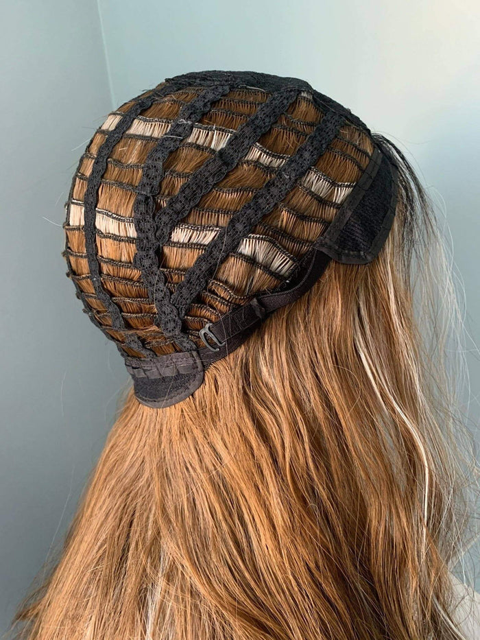 Black lace front wig cap on a person with long blonde hair against a light blue background