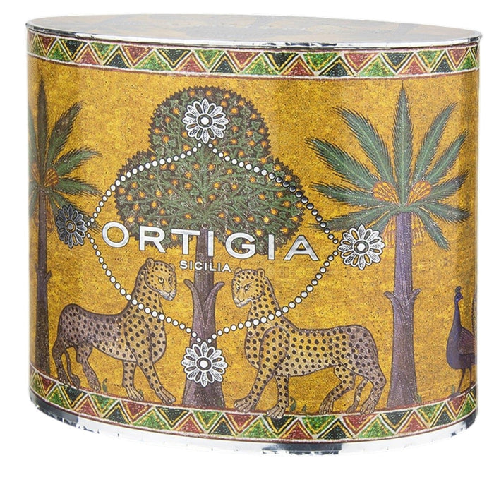 The ORTIGIA SICILIA - ZAGARA OVAL GIFT SET by ORTIGIA SICILIA features products infused with the refreshing scent of Sicilian orange blossoms, including a bottle, tube, soap, and candle. Each item is adorned with palm tree and leopard motifs and elegantly arranged on a shiny tray in front of an ornate yellow gift box.