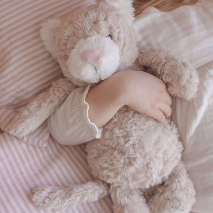 Child holding a teddy bear on a pink striped blanket