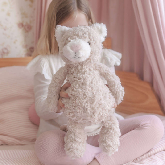 Child holding a teddy bear in a bedroom setting with pink curtains and bedding.