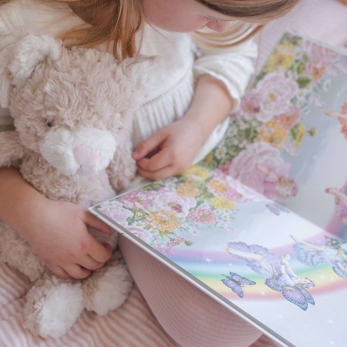 Child reading a colorful book with a teddy bear on a pink bed.