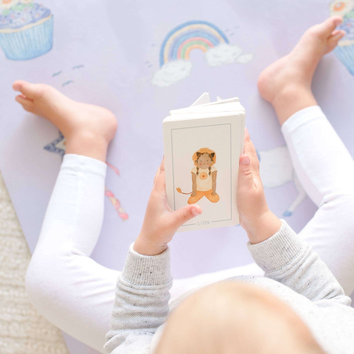 Child holding a book with a lion illustration on a colorful floor mat.