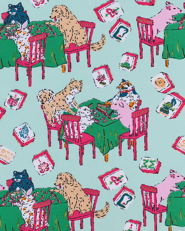 Dressed in PRINTFRESH’s Mahjong Menagerie Pajama Short Set, this person sports matching pastel organic cotton sleepwear featuring a playful cat print with tables, books, and chairs. The set includes a short-sleeve button-up shirt and shorts, both finished with light pink trim.