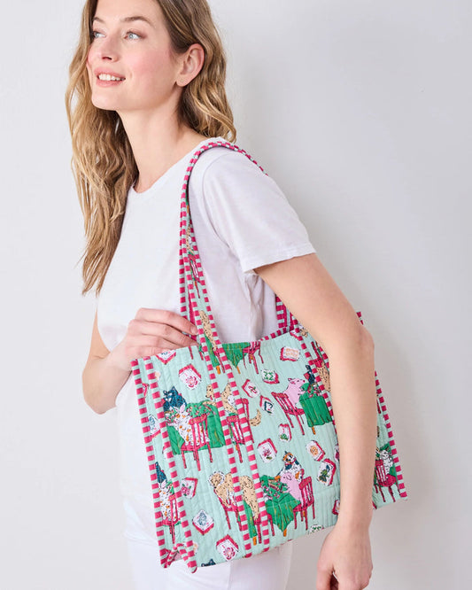 The PRINTFRESH - MAHJONG MENAGERIE TRAVELER TOTE by PRINTFRESH is an organic cotton tote bag adorned with a playful animal print on a light blue background and finished with pink-and-white striped handles. Hanging on a wooden wall hook, this charming and whimsical tote combines everyday functionality with unique style.